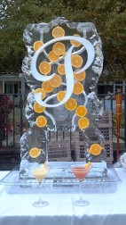 Oranges frozen into block of double pour drink luge with large script snowfilled initial, rocky edges